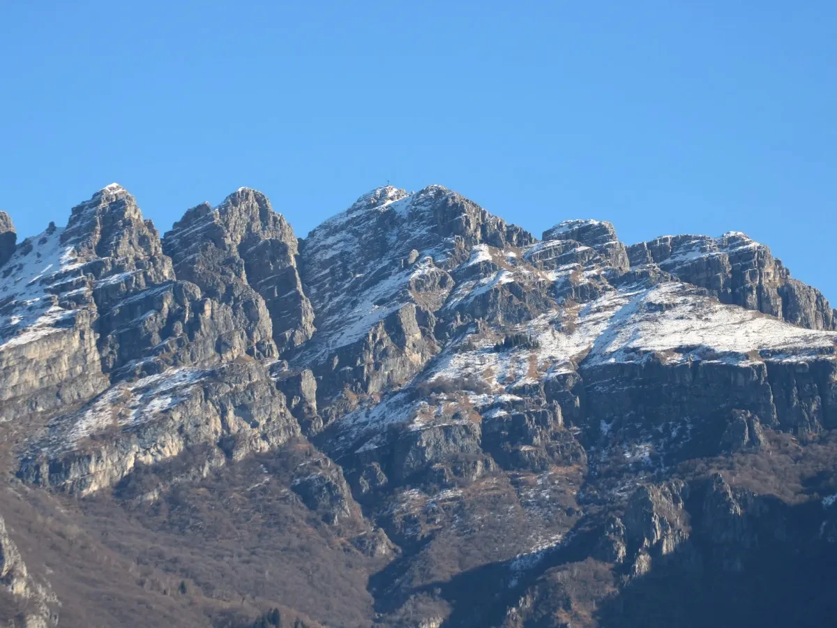 Breathtaking view of snow-covered mountain peaks in Lombardy, Italy under a clear blue sky.