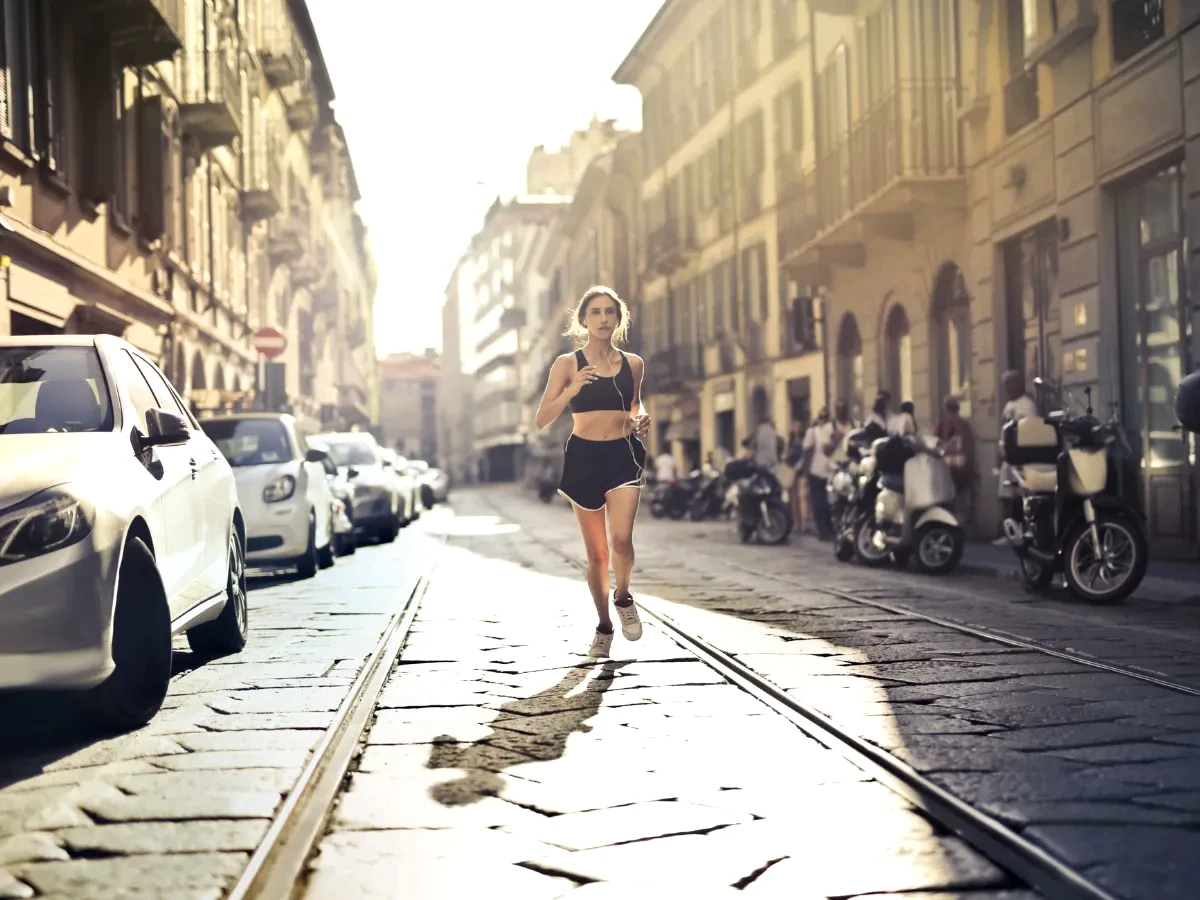 Energetic woman jogger running down a city street in active wear on a sunny day.